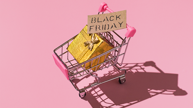 Metal shopping cart with black friday sign and golden gift box with hard shadow, on pink background.